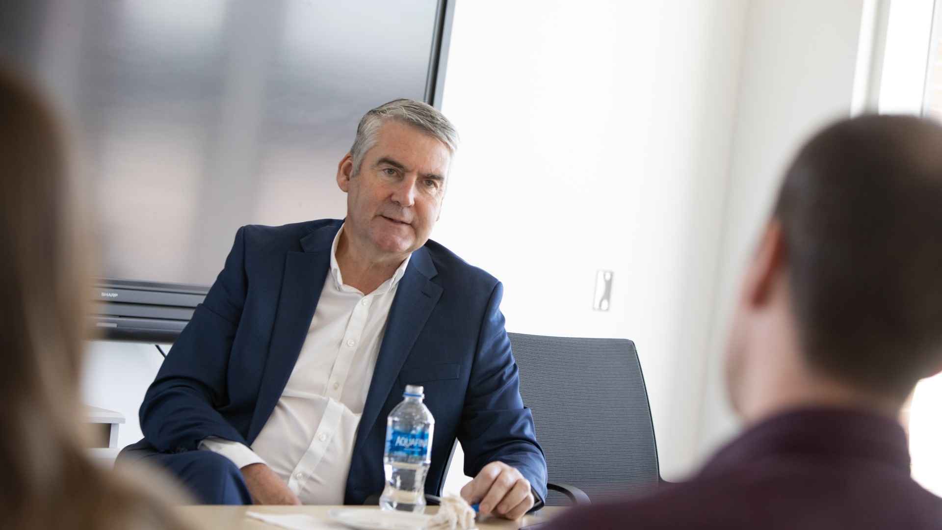 A man in a suit speaking with two students at a table