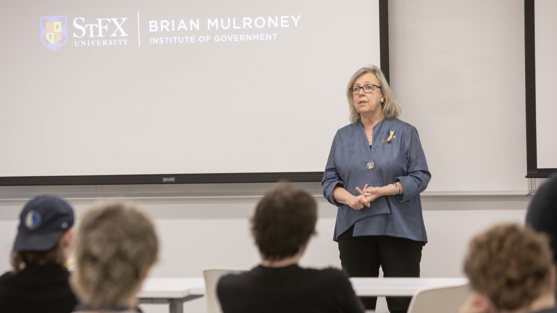 A woman giving a lecture in a classroom in front of a projector screen