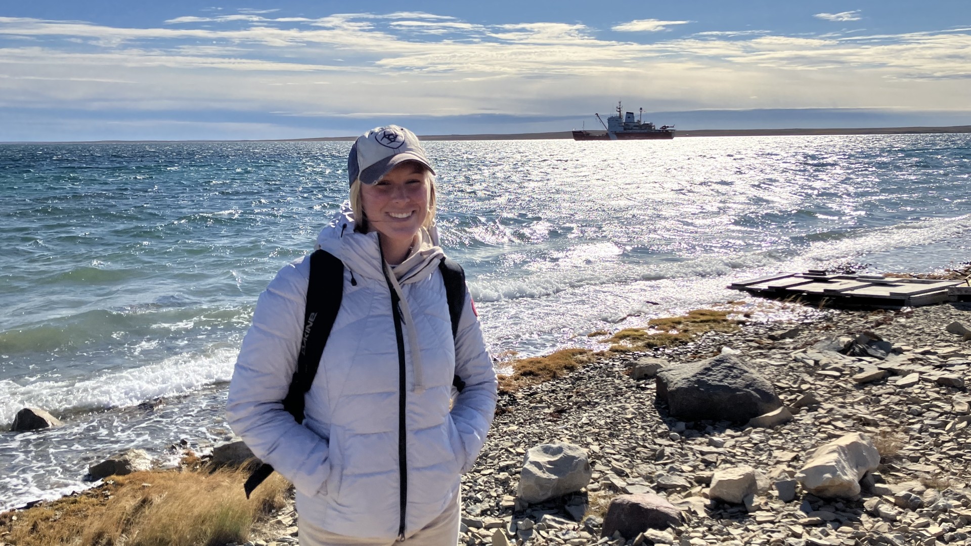 A young woman standing on a beach with a ship in the background