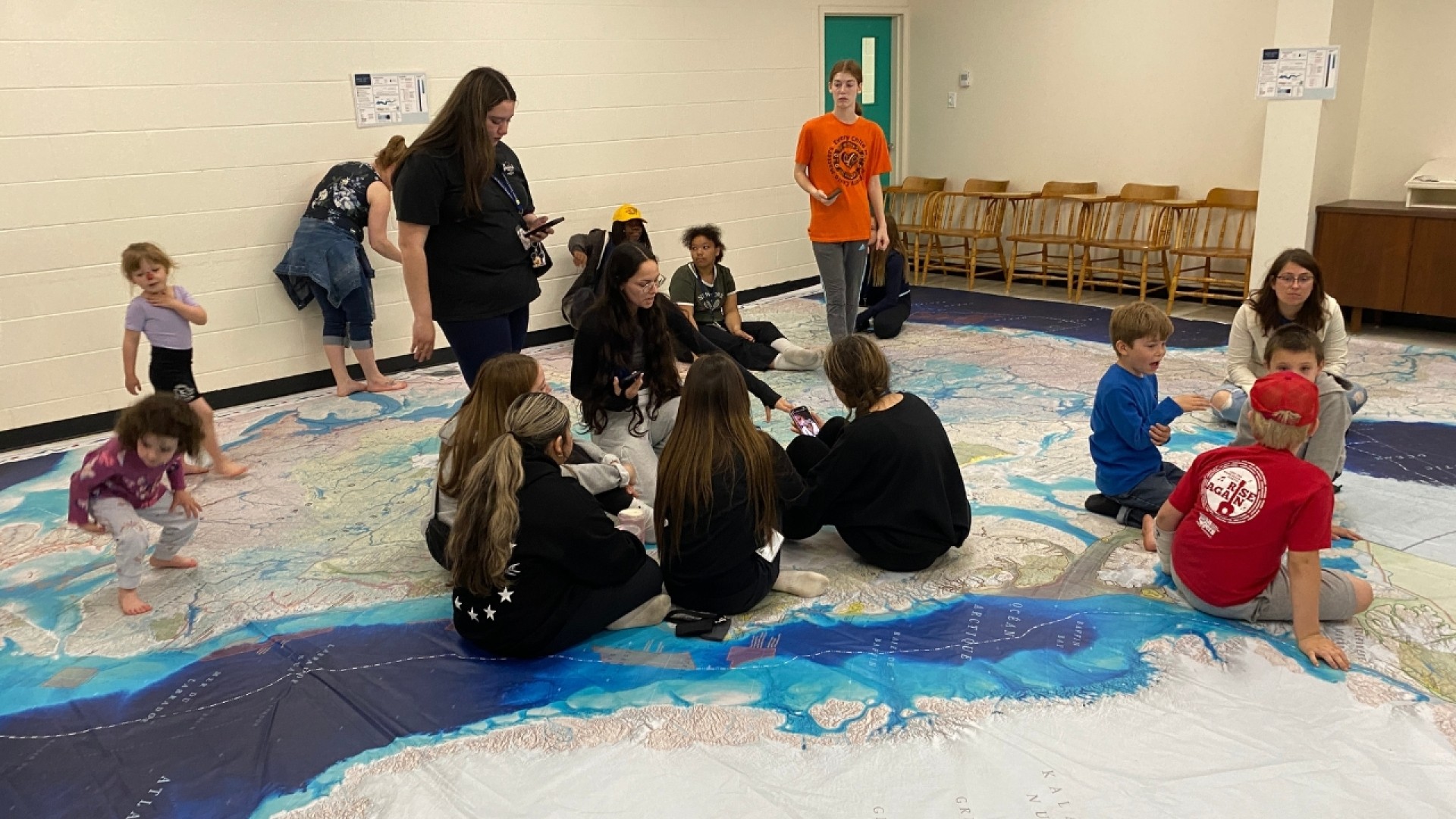 Children and adults interacting on a large floor map of the Atlantic Ocean in a classroom setting.