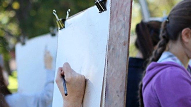 Student sketching outdoors with others drawing in the background, representing the StFX Bachelor of Arts in Art program.