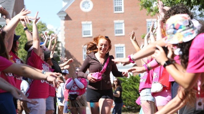 A happy student runs between two lines of cheering people in pink shirts