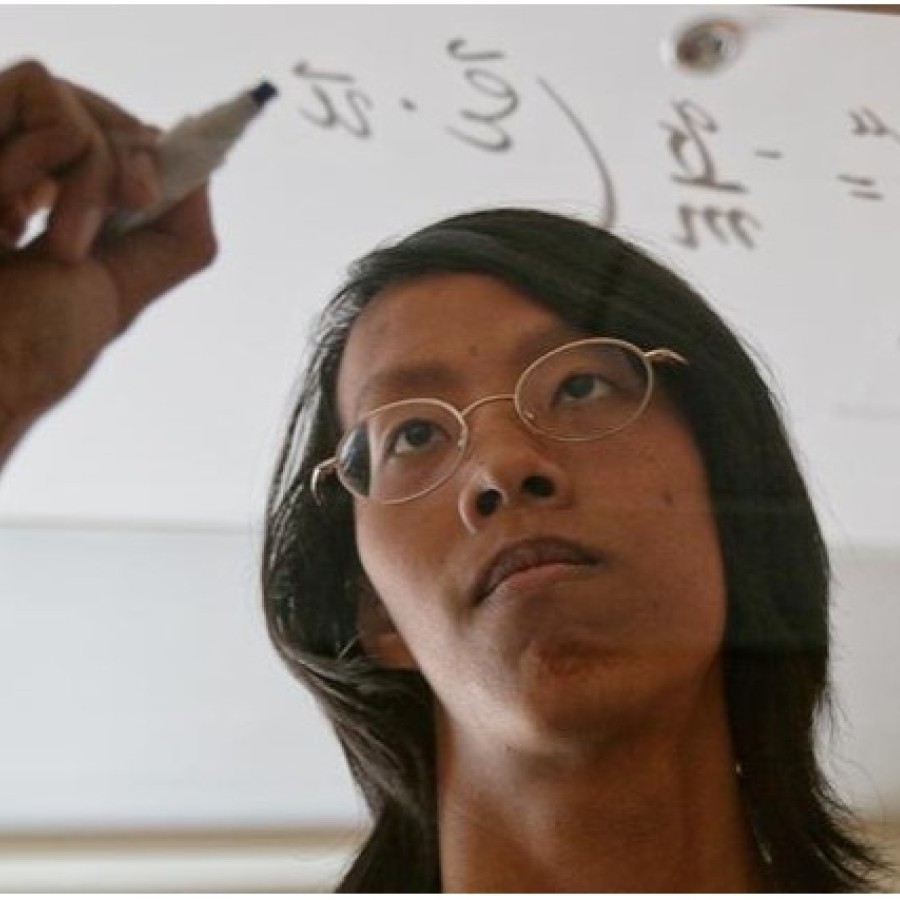 A student is writing math formula on the transparent glass board. 