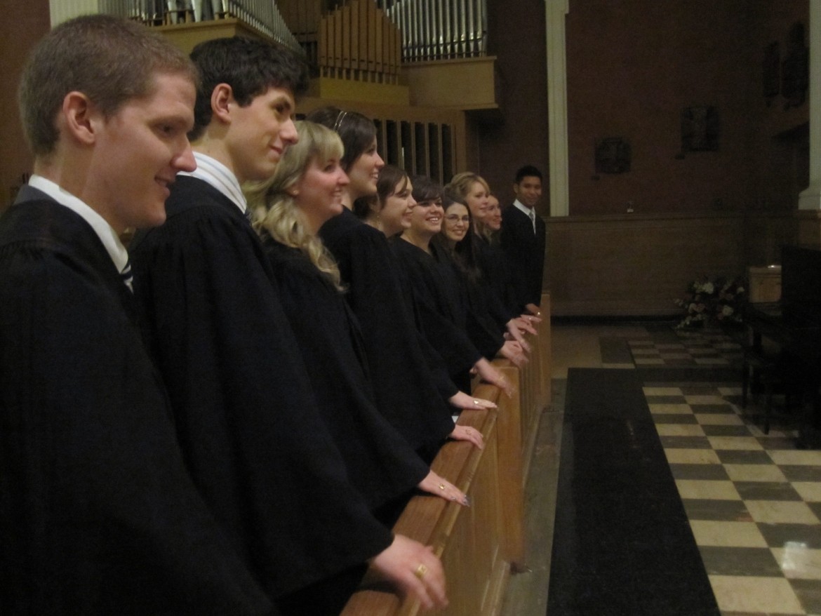 People wearing black gowns standing in a church pew