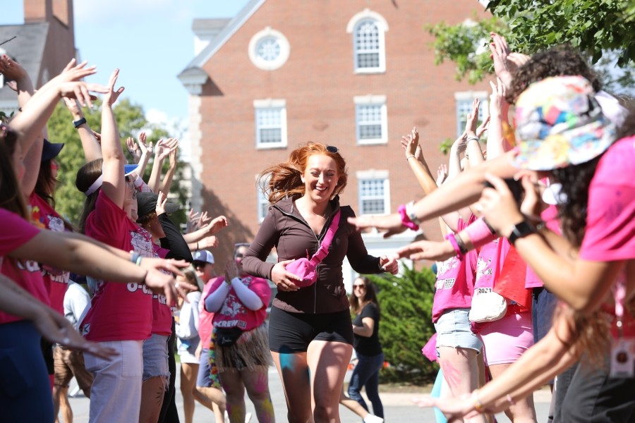 A happy student runs between two lines of cheering people in pink shirts