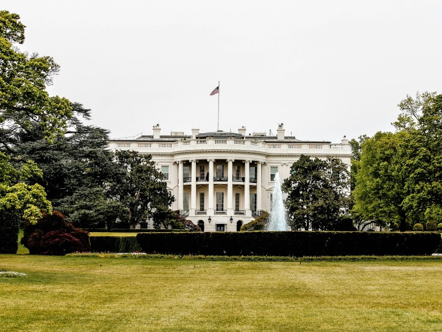 Photo of the White House, a multi-storey building with columns and an American flag on its roof. 